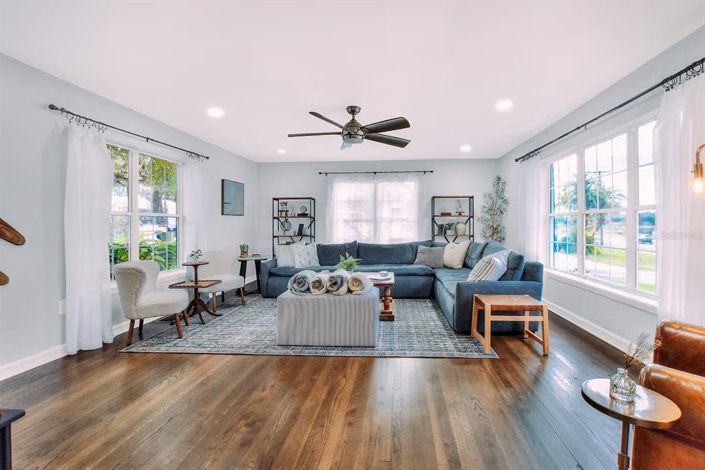 A living room features a blue sectional sofa, hardwood floors, and large windows with curtains — 1302 LAKE ELBERT DR SE, WINTER HAVEN, FL