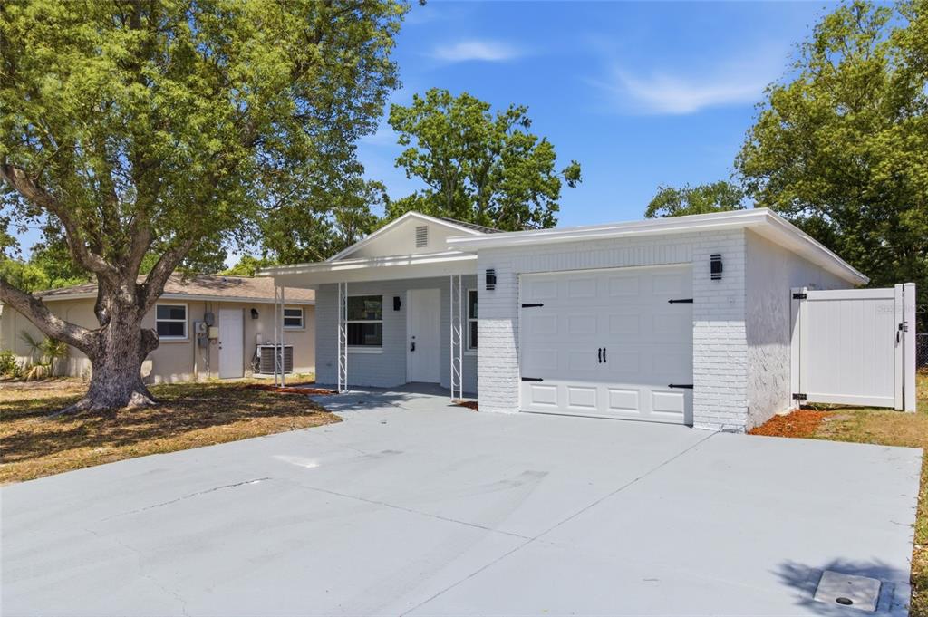 A light gray painted brick house features a white garage door and a concrete driveway — 3042 BAHIA AVENUE, HOLIDAY, FL