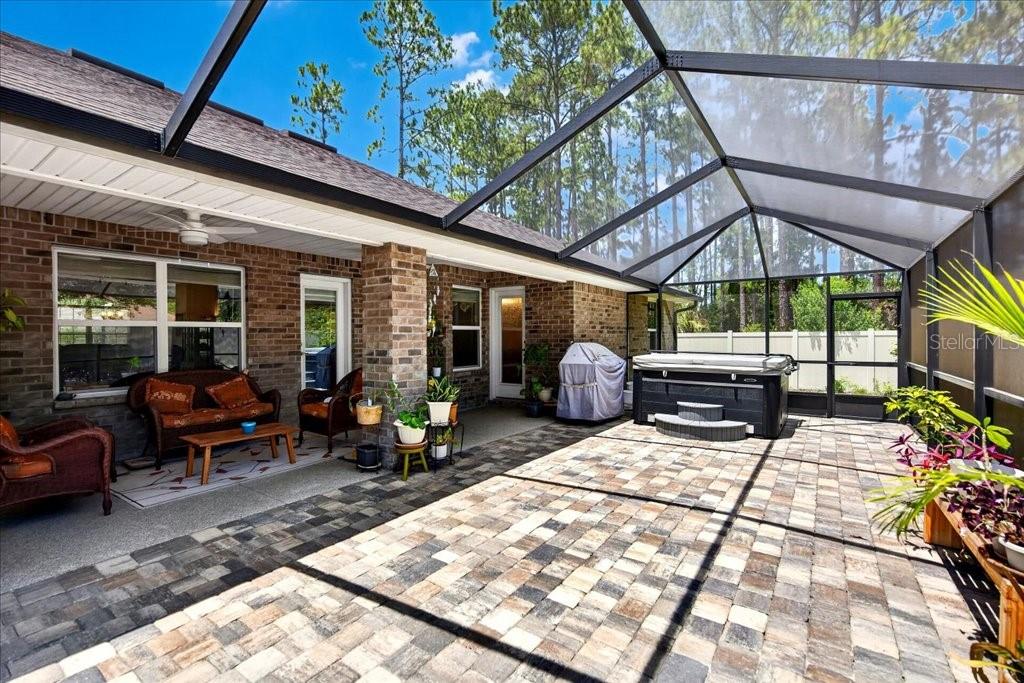 A screened-in patio features brick walls, paver flooring, a hot tub, and outdoor furniture — 118 RYBERRY DRIVE, PALM COAST, FL