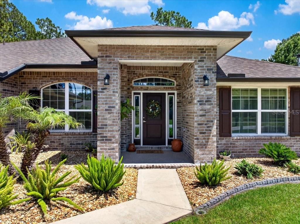 The exterior of a brick house features a covered entryway with a dark front door — 118 RYBERRY DRIVE, PALM COAST, FL