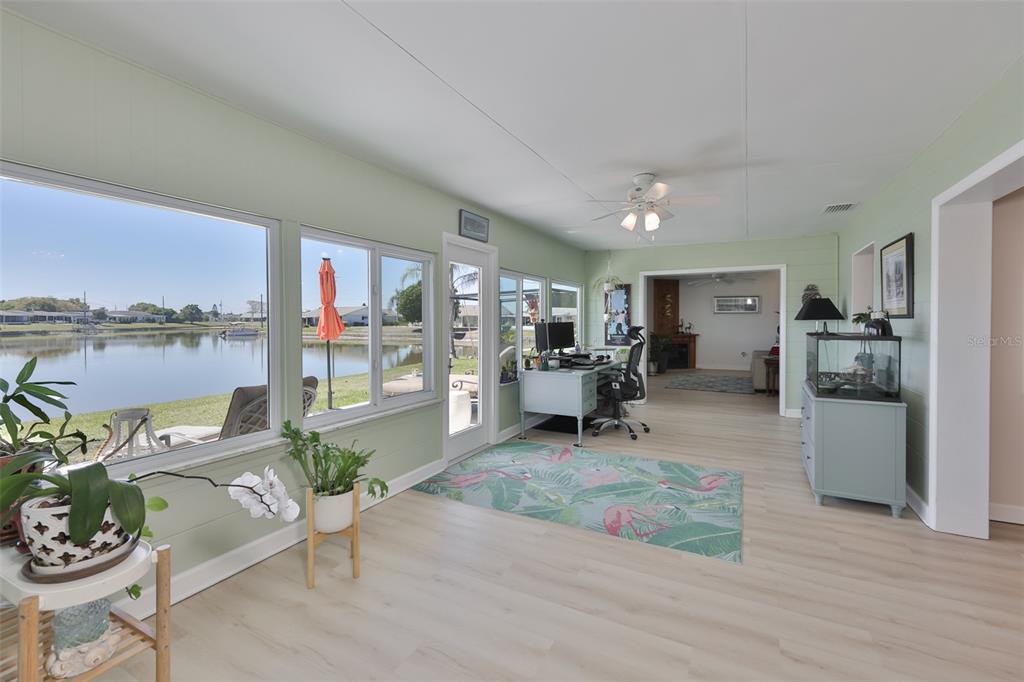 A sunroom with light green walls, wood-look flooring, and large windows overlooking a lake — 1704 DANBURY DRIVE, SUN CITY CENTER, FL