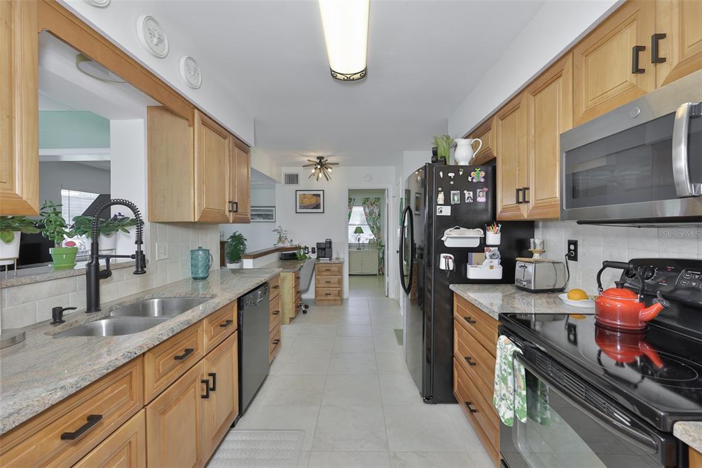 A galley kitchen features light wood cabinets, granite countertops, and black appliances — 1704 DANBURY DRIVE, SUN CITY CENTER, FL