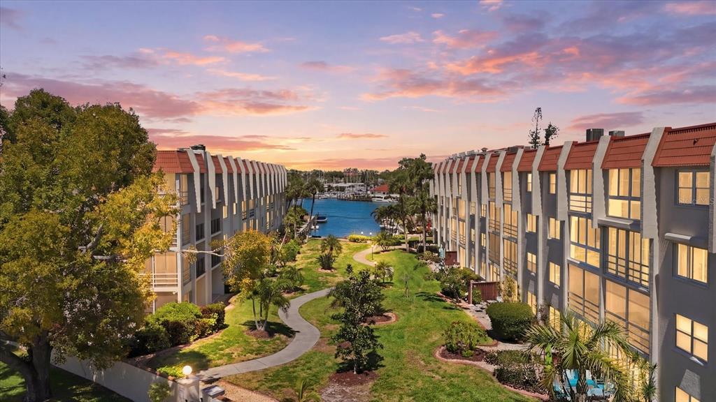 An exterior view of two multi-story apartment buildings flanking a grassy courtyard leading to water — 220 SANTA MARIA STREET UNIT 342, VENICE, FL