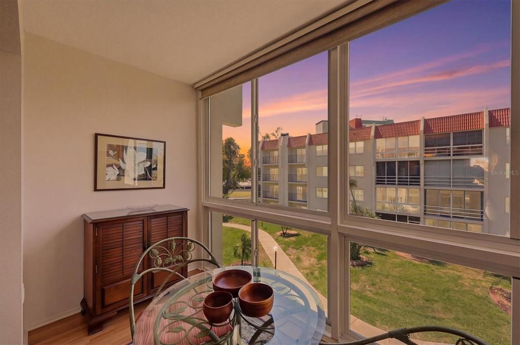 A dining area with a glass table and wooden cabinet overlooks a courtyard at sunset — 220 SANTA MARIA STREET UNIT 342, VENICE, FL
