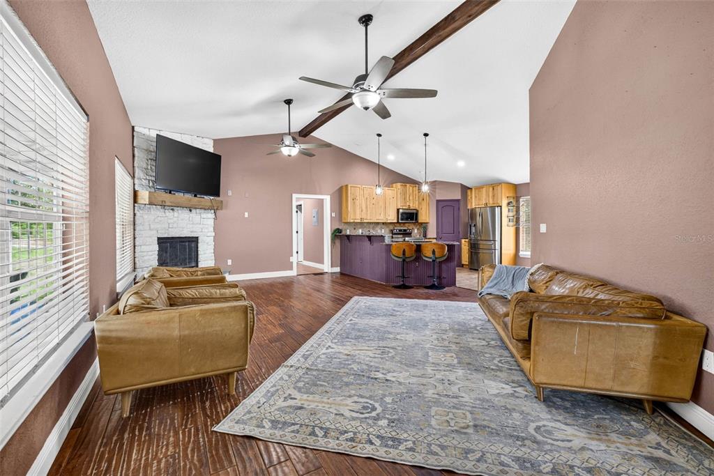 A living room with wood floors, a stone fireplace, and an open kitchen with bar seating — 4243 NANCY CREEK BOULEVARD, BROOKSVILLE, FL