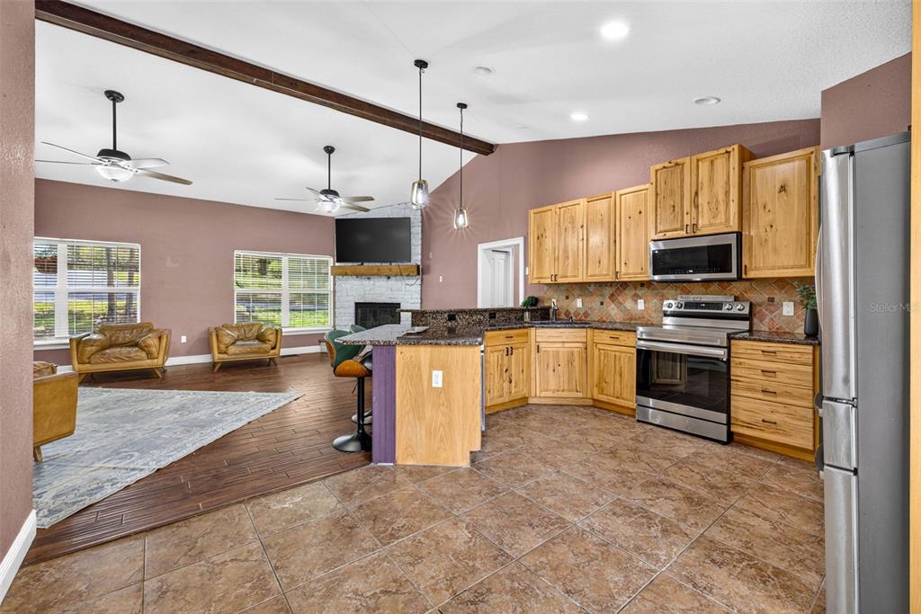 An open-concept kitchen and living area featuring wood cabinets, tile flooring, and a stone fireplace — 4243 NANCY CREEK BOULEVARD, BROOKSVILLE, FL