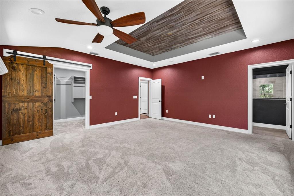 A bedroom with red walls, gray carpet, a wood-paneled tray ceiling, and a barn door — 4243 NANCY CREEK BOULEVARD, BROOKSVILLE, FL