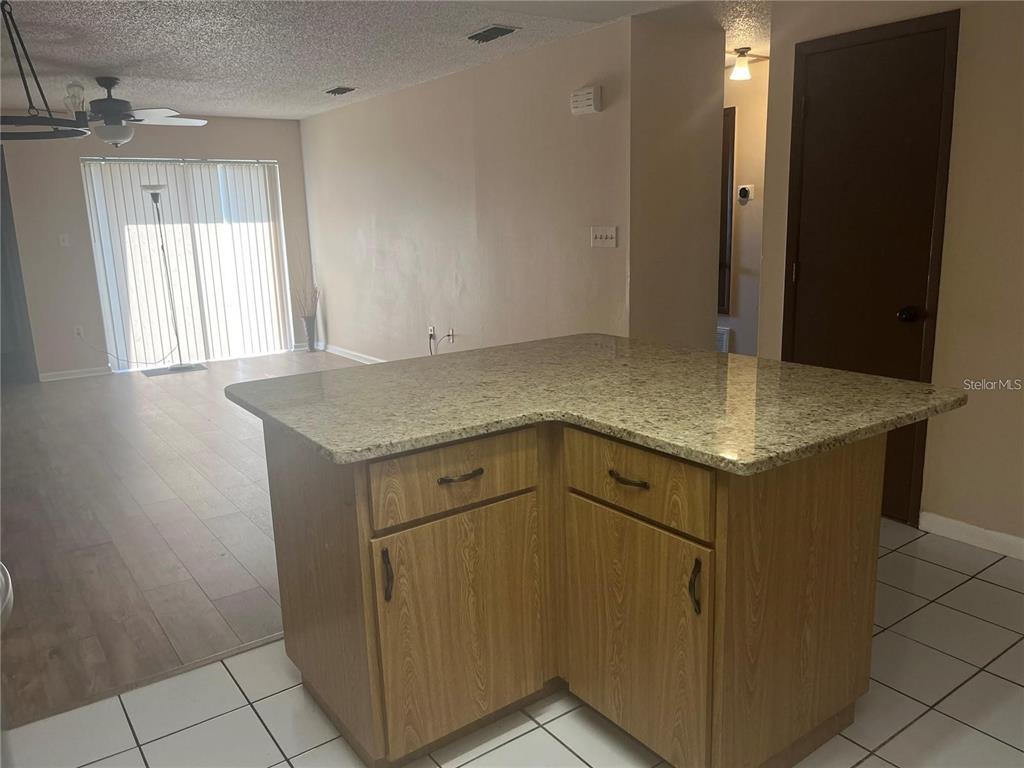 A kitchen island with a granite countertop sits in front of a living area — 2112 W MARTIN STREET, KISSIMMEE, FL