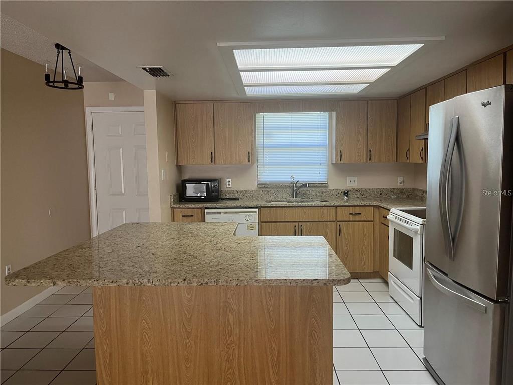 A kitchen features light wood cabinets, granite countertops, stainless steel appliances, and a central island — 2112 W MARTIN STREET, KISSIMMEE, FL