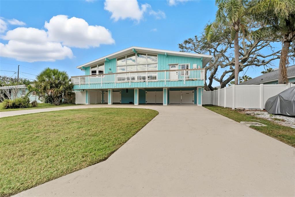 A light blue elevated house with a large front deck and a concrete driveway — 208 BATES AVENUE, INDIAN ROCKS BEACH, FL