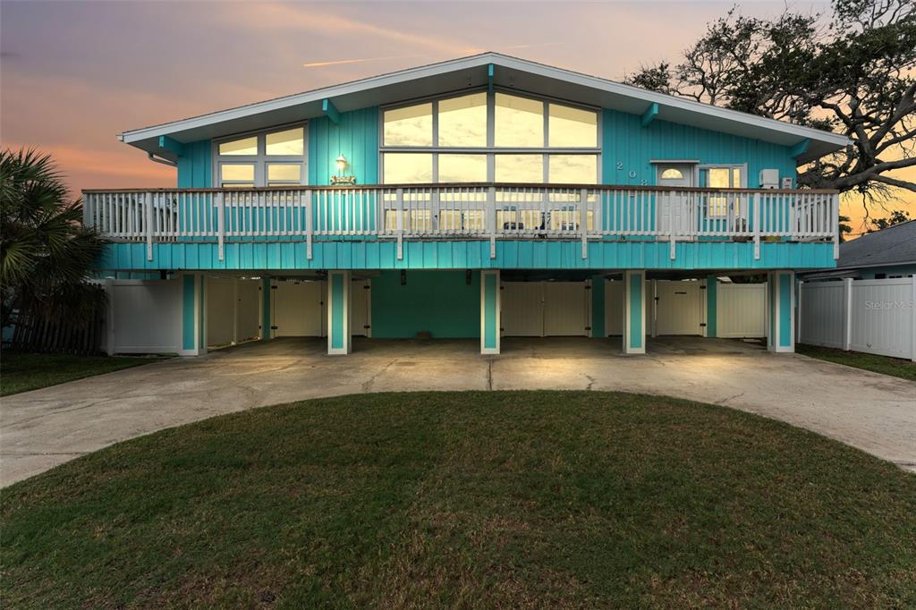 A teal elevated house with a large deck and a concrete driveway at dusk — 208 BATES AVENUE, INDIAN ROCKS BEACH, FL