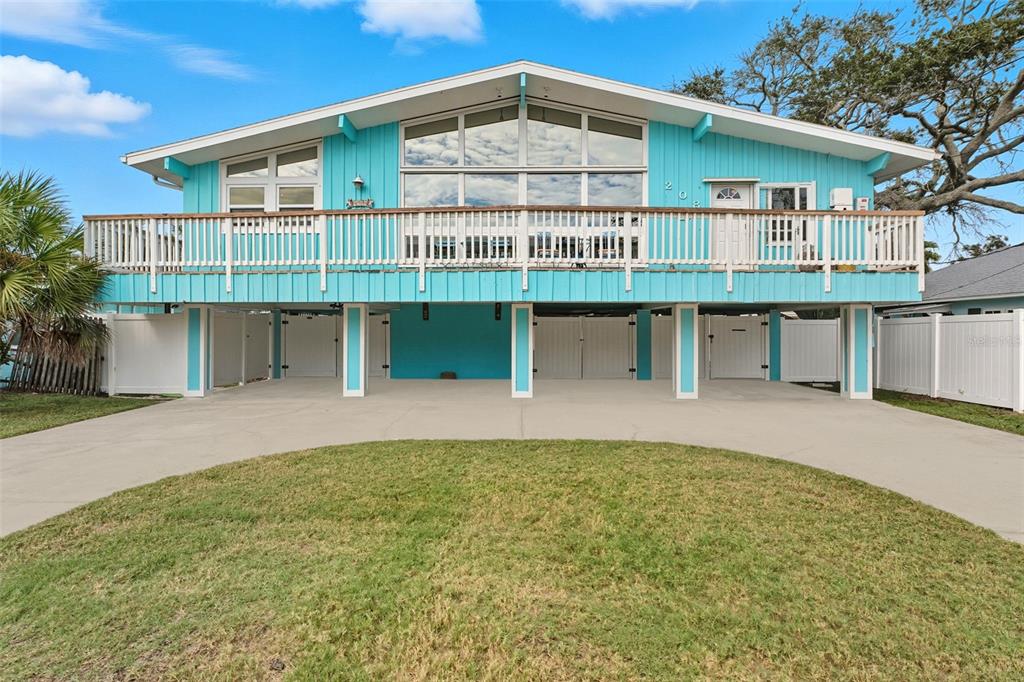 A bright blue elevated house with a large deck and a concrete driveway below — 208 BATES AVENUE, INDIAN ROCKS BEACH, FL