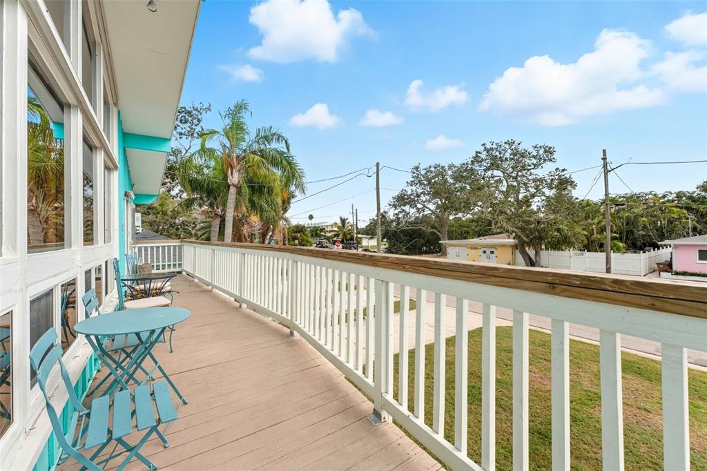 A wooden balcony with blue bistro furniture overlooks a residential street and palm trees — 208 BATES AVENUE, INDIAN ROCKS BEACH, FL