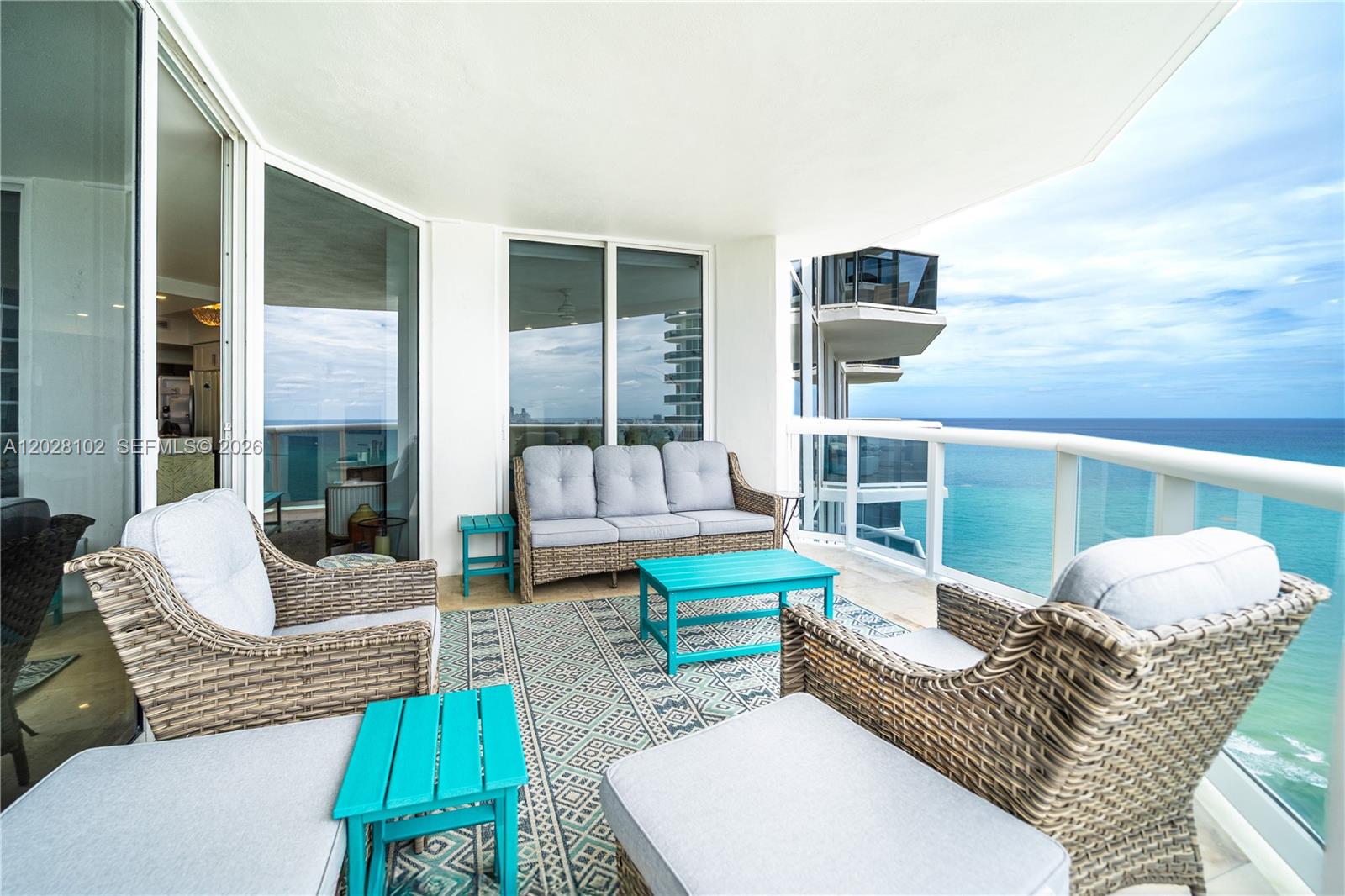 A balcony features wicker furniture, teal tables, and a patterned rug overlooking the ocean — 4779 Collins Ave # 3504, Miami Beach FL 33140, MIAMI BEACH, FL
