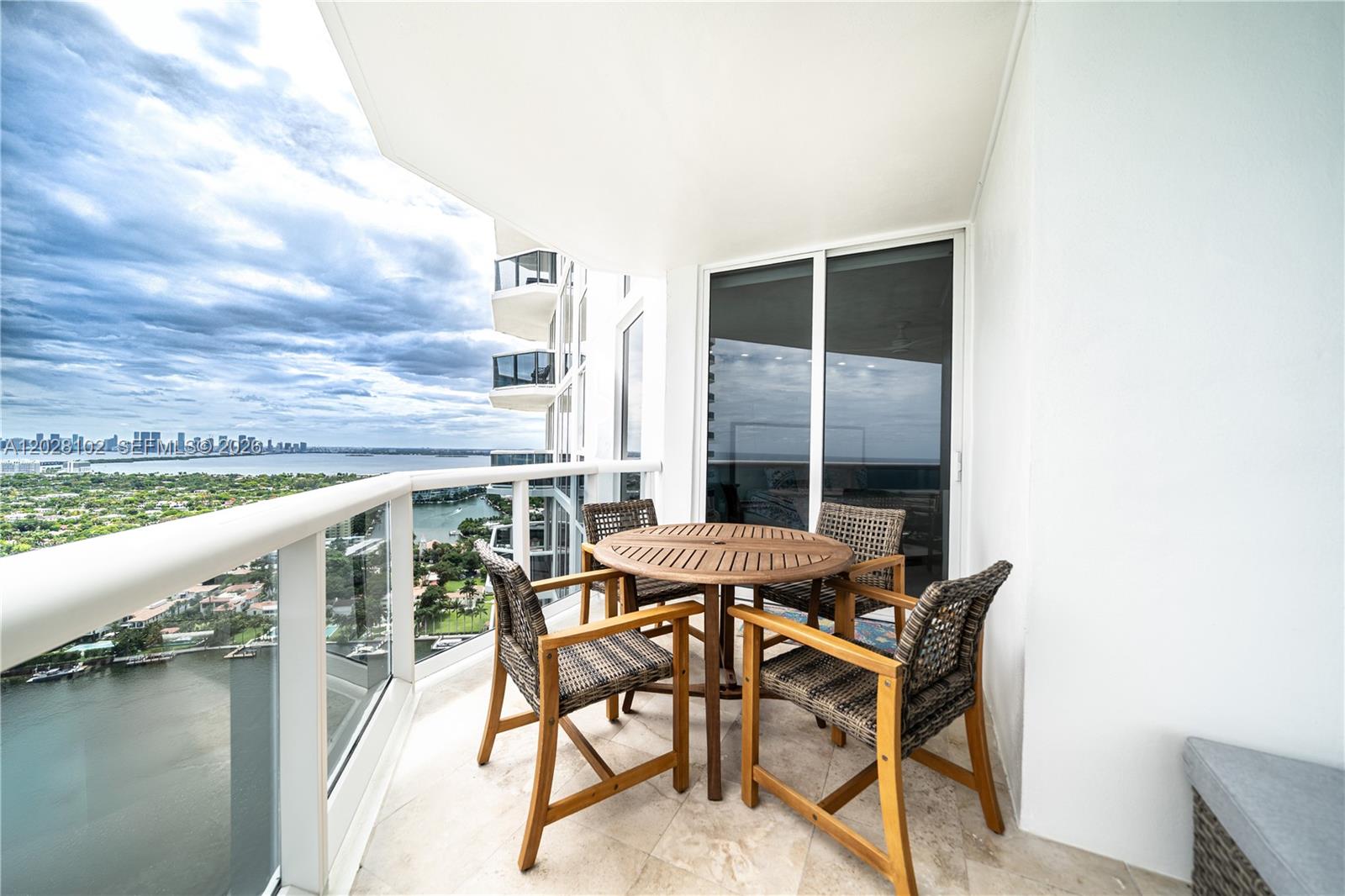 A balcony features a round wooden table with four wicker chairs overlooking a waterfront view — 4779 Collins Ave # 3504, Miami Beach FL 33140, MIAMI BEACH, FL