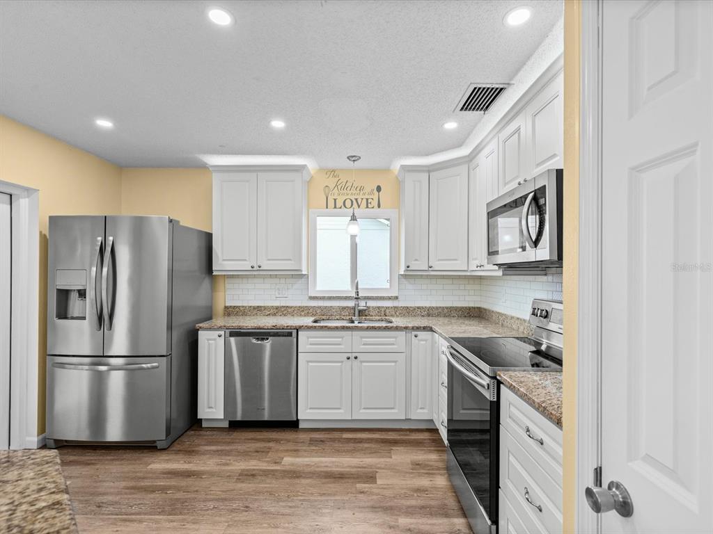 A kitchen with white cabinets, stainless steel appliances, granite countertops, and wood-look flooring — 1105 TUXFORD DRIVE, BRANDON, FL