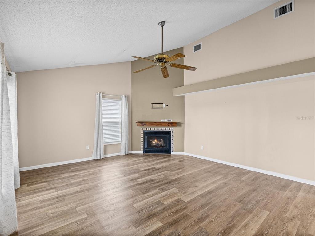 A living room features wood-look flooring, a vaulted ceiling with a fan, and a fireplace — 1105 TUXFORD DRIVE, BRANDON, FL