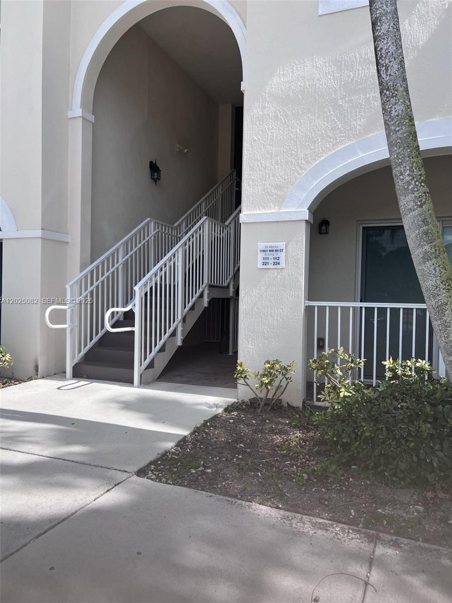 An exterior view shows a beige building entrance with a staircase and white railings — 11601 NW 89th St # 222, Doral FL 33178, DORAL, FL