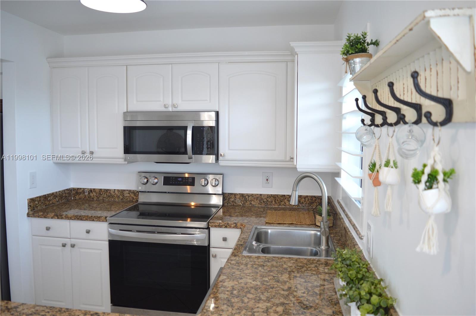 A kitchen features white cabinets, granite countertops, stainless steel appliances, and a wall-mounted coat rack — 1511 SE 15th Ct # 403, Deerfield Beach FL 33441, DEERFIELD BEACH, FL