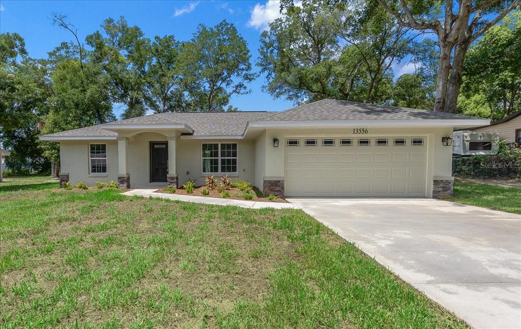 A single-story house with a beige stucco exterior, a two-car garage, and a front walkway — 13556 SE 102ND COURT, BELLEVIEW, FL