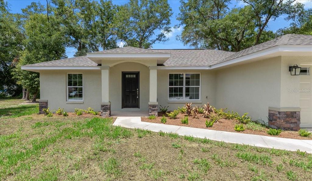 A single-story house exterior features a covered entryway, stone-accented columns, and a concrete walkway — 13556 SE 102ND COURT, BELLEVIEW, FL