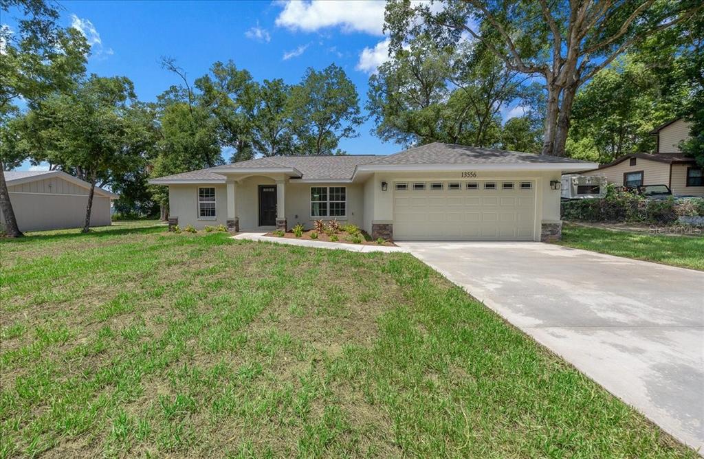 A single-story house with a beige exterior, a two-car garage, and a concrete driveway — 13556 SE 102ND COURT, BELLEVIEW, FL