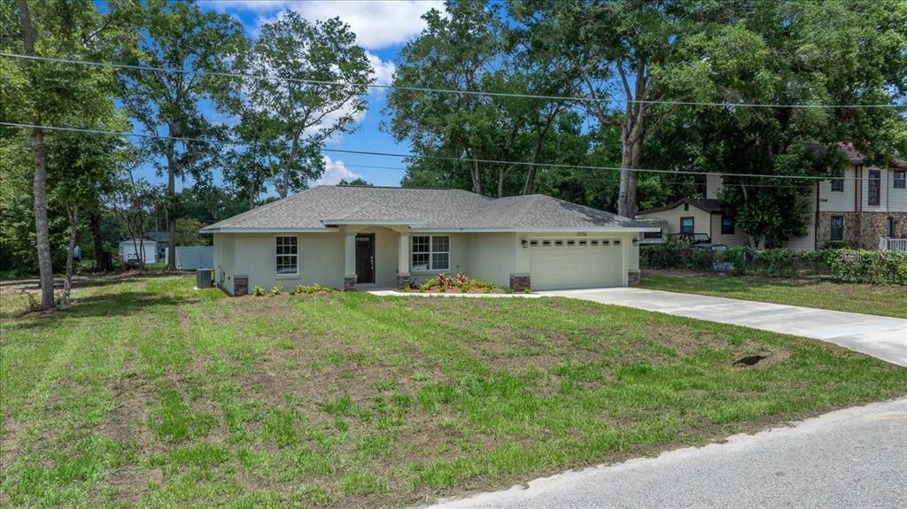 A single-story house with a light-colored exterior, a two-car garage, and a grassy front yard — 13556 SE 102ND COURT, BELLEVIEW, FL