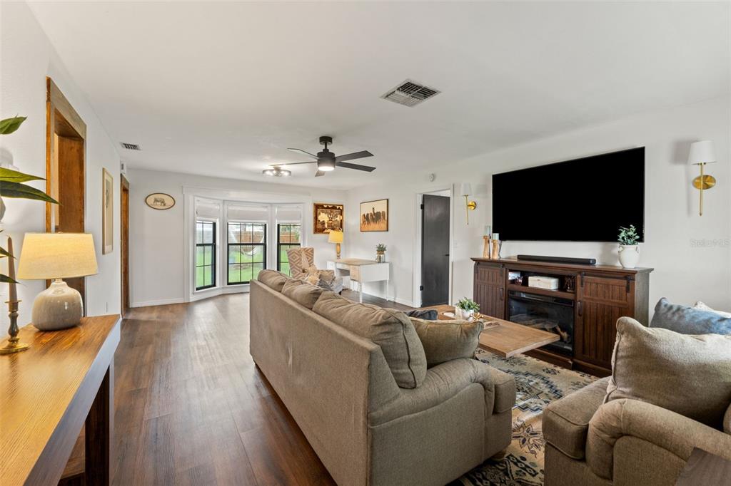 A living room features a large television, a sofa, wood flooring, and a bay window — 8449 VALMORA STREET, SPRING HILL, FL