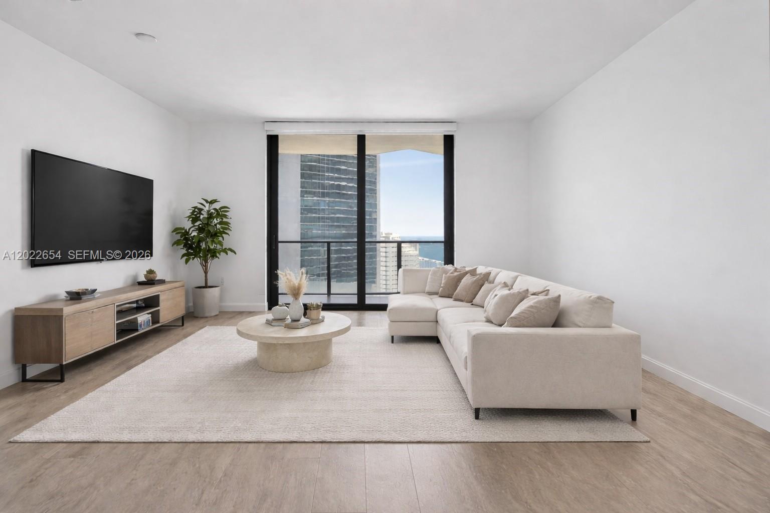 A modern living room features a sectional sofa, a circular coffee table, and a television — 45 SW 9th St # 3502, Miami FL 33130, MIAMI, FL