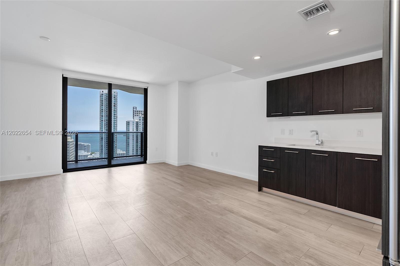 A modern kitchen area with dark cabinets and light wood floors overlooks a city skyline — 45 SW 9th St # 3502, Miami FL 33130, MIAMI, FL