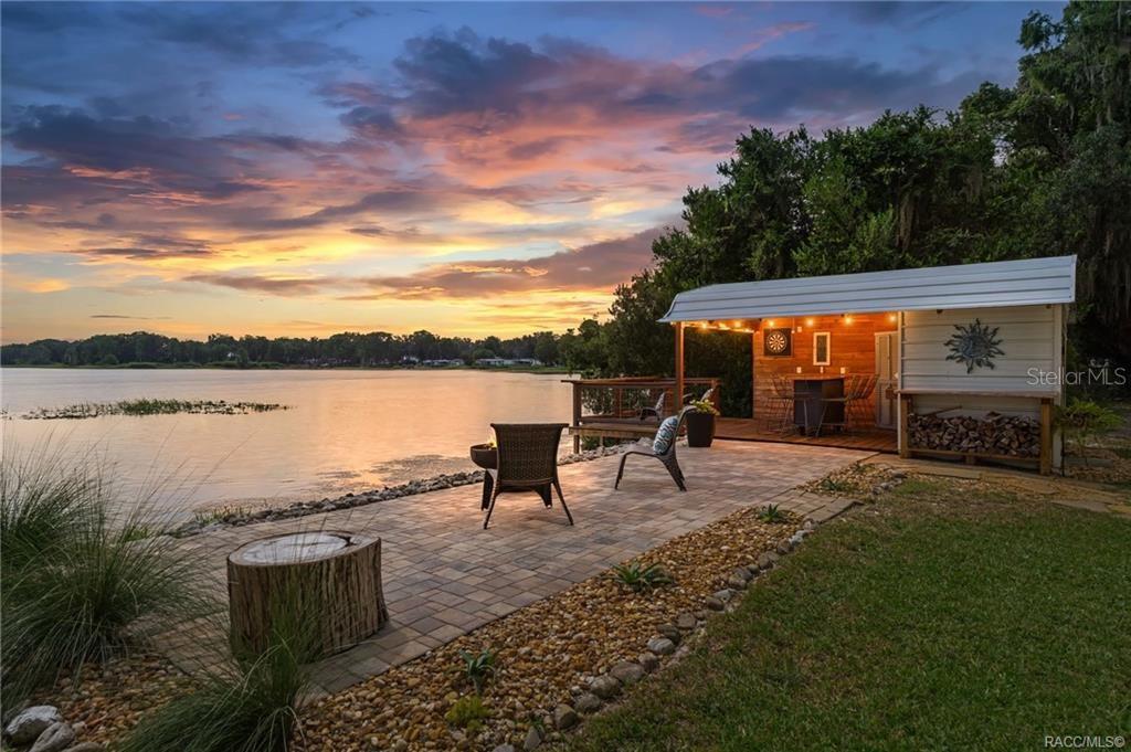 A paved patio with outdoor seating overlooks a lake at sunset next to a small shed — 412 ELLA AVENUE, INVERNESS, FL