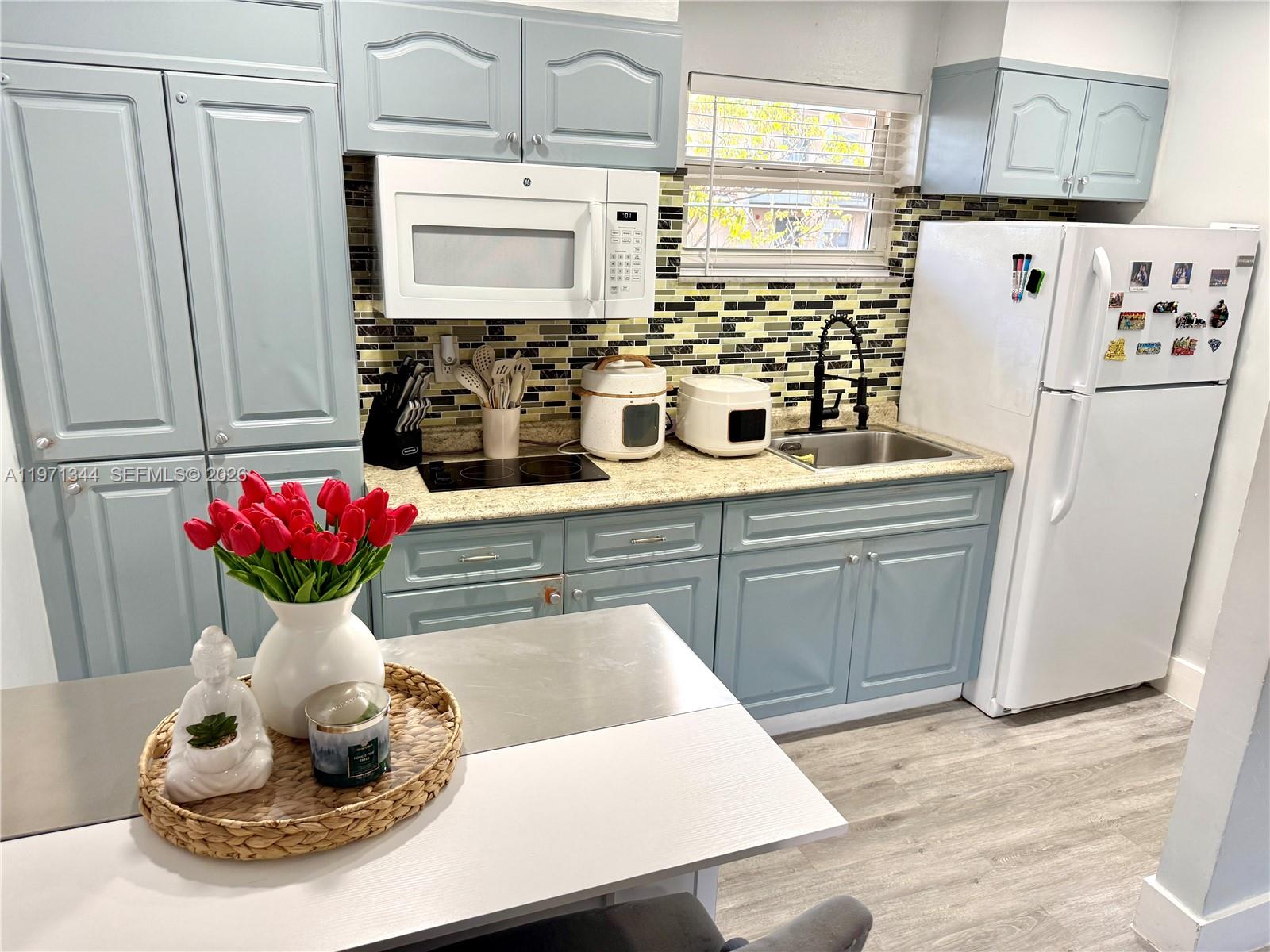 A kitchen features blue cabinets, a white microwave, a white refrigerator, and a tiled backsplash — 399 NW 72nd Ave # 210, Miami FL 33126, MIAMI, FL