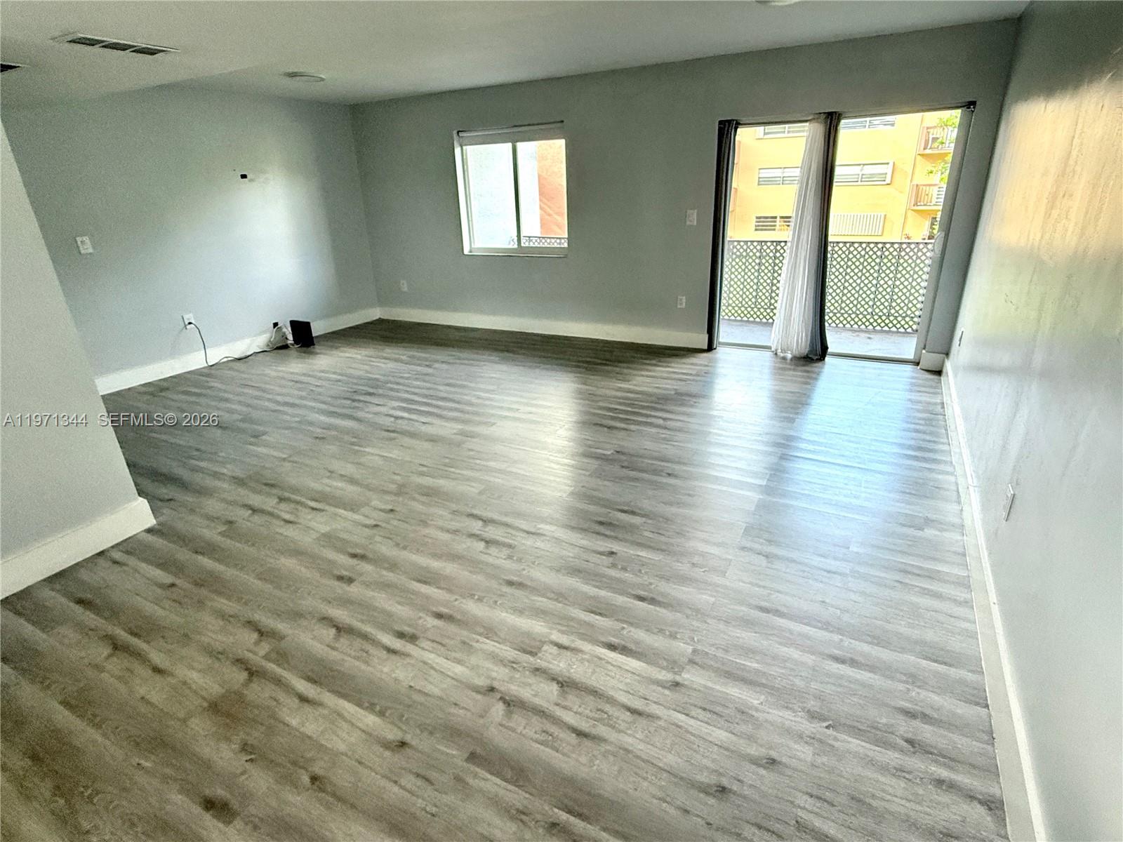 An unfurnished living room features gray walls, wood-look flooring, a window, and a sliding door — 399 NW 72nd Ave # 210, Miami FL 33126, MIAMI, FL