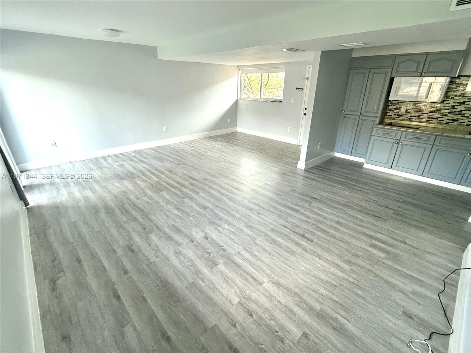 An open-concept room features gray wood-look flooring, light gray walls, and a small kitchenette — 399 NW 72nd Ave # 210, Miami FL 33126, MIAMI, FL