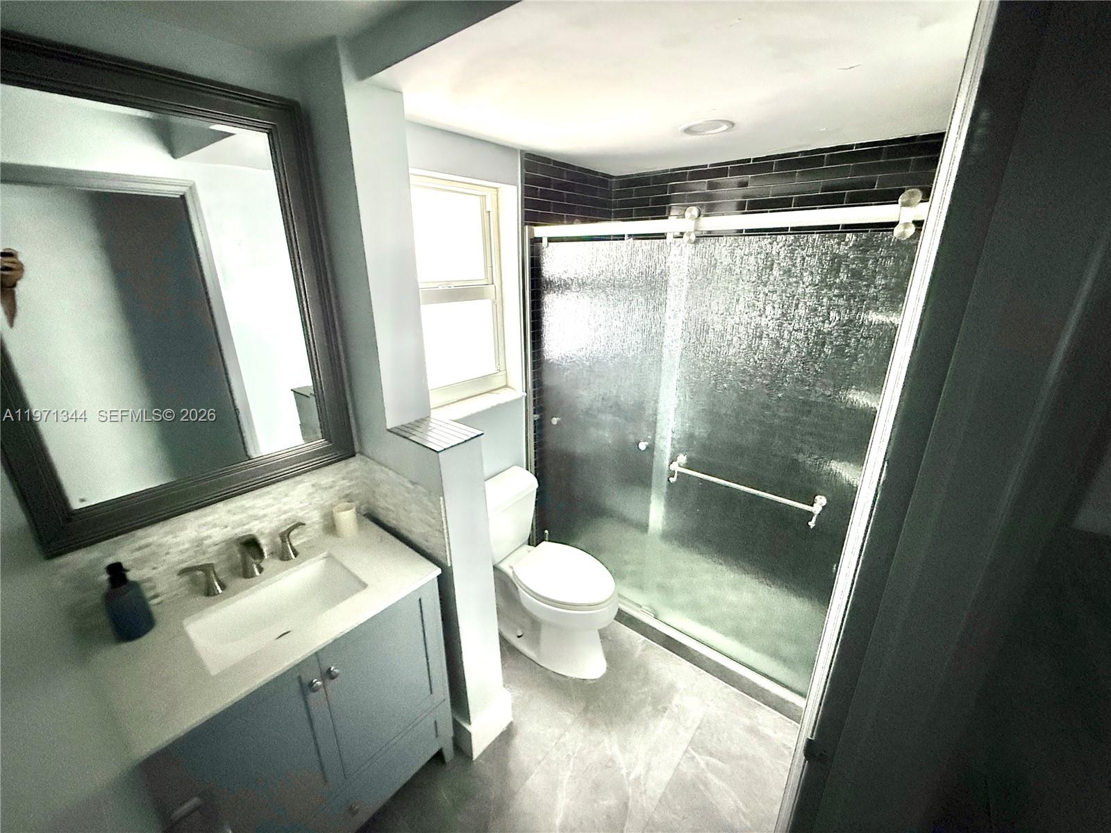 A bathroom features a gray vanity, a toilet, and a glass-enclosed shower with dark tiles — 399 NW 72nd Ave # 210, Miami FL 33126, MIAMI, FL