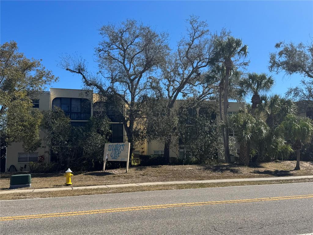 A multi-story apartment building stands behind a sign and trees next to a road — 11485 OAKHURST ROAD UNIT -211, LARGO, FL
