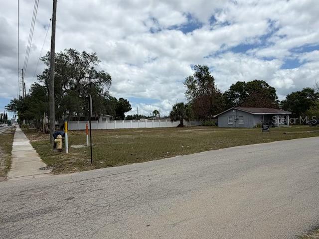 A vacant grassy lot sits next to a single-story house under a cloudy sky — 401 E GREEN STREET, AVON PARK, FL