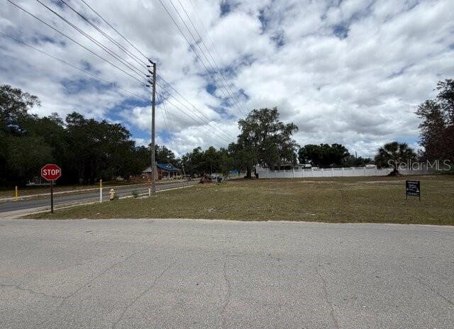 A vacant, grassy lot sits at a street corner with a stop sign and utility pole — 401 E GREEN STREET, AVON PARK, FL