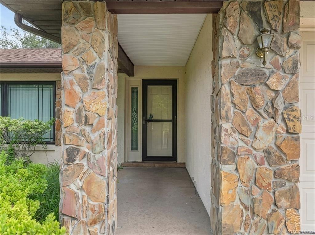 A covered entryway features stone-clad pillars, a glass storm door, and a side light window — 206 HEMLOCK STREET, INVERNESS, FL