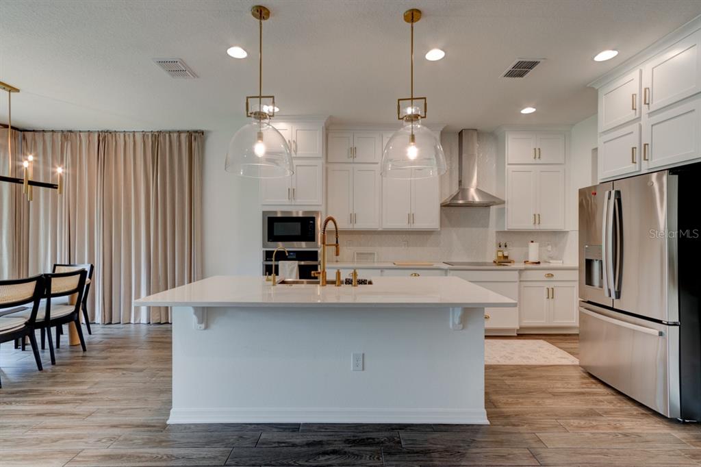 A kitchen features a white island, stainless steel appliances, white cabinetry, and two glass pendant lights — 5675 GREEN ARROW PLACE, SANFORD, FL