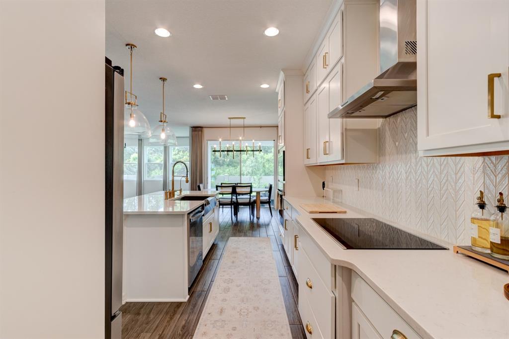 A modern kitchen features white cabinetry, quartz countertops, a center island, and stainless steel appliances — 5675 GREEN ARROW PLACE, SANFORD, FL