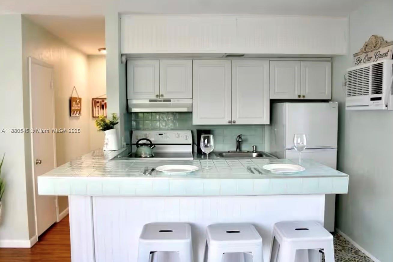 A kitchen features white cabinets, a tiled countertop, and a breakfast bar with three stools — 316 Walnut St # 2, Hollywood FL 33019, HOLLYWOOD, FL