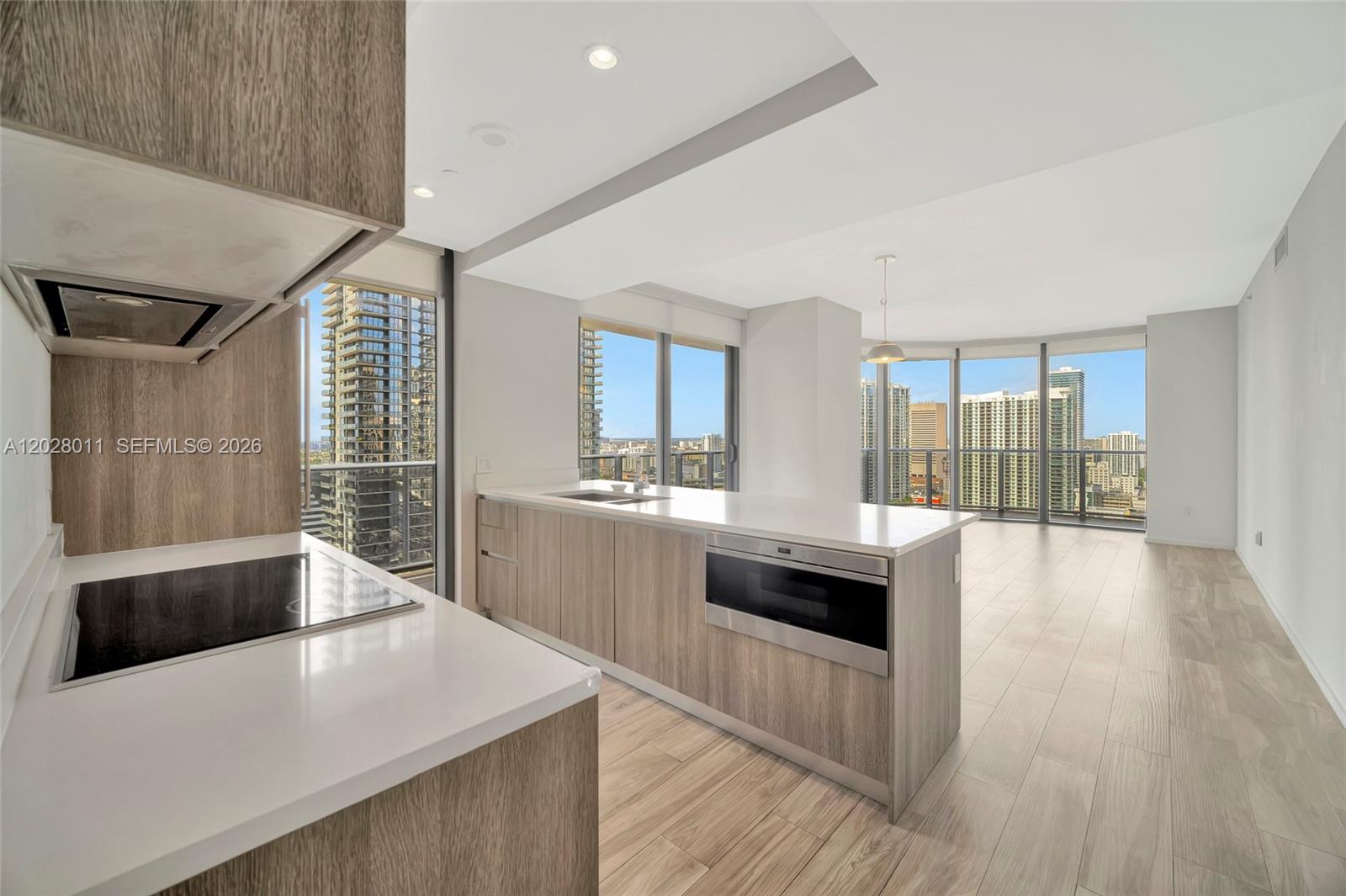 A modern kitchen with light wood cabinetry and white countertops overlooks a high-rise city view — 801 S Miami Ave # 2909, Miami FL 33130, MIAMI, FL