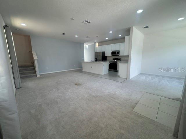 An open-concept living area features a kitchen with white cabinets, stainless appliances, and carpeted floors — 269 BELLA PRESTWICK BOULEVARD, DAVENPORT, FL