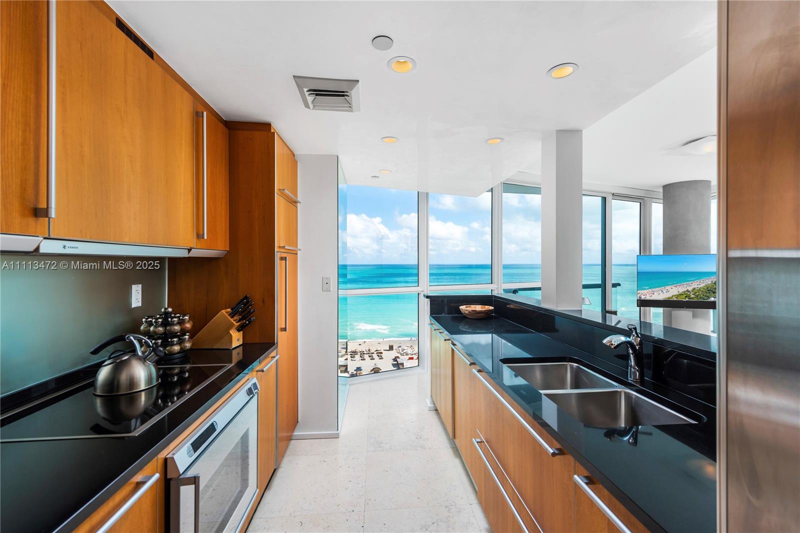 A modern kitchen features wood cabinetry, black countertops, and floor-to-ceiling windows overlooking the ocean — 101 20th St # 2208, Miami Beach FL 33139, MIAMI BEACH, FL