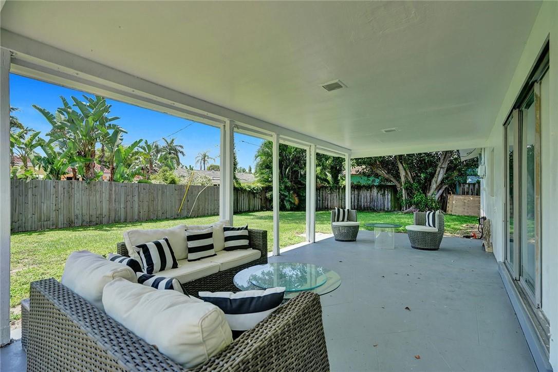A covered patio with wicker furniture overlooks a grassy backyard enclosed by a wooden fence — 5101 NE 27th Avenue, Lighthouse Point FL 33064, LIGHTHOUSE POINT, FL