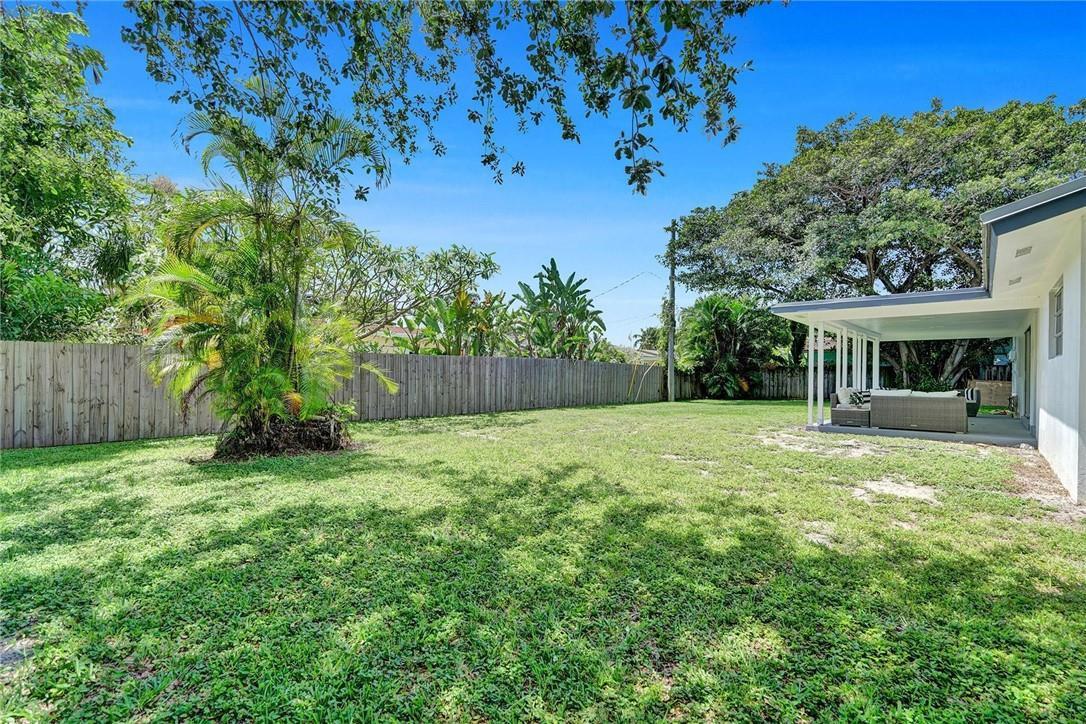 A grassy backyard features a wooden fence, a palm tree, and a covered patio area — 5101 NE 27th Avenue, Lighthouse Point FL 33064, LIGHTHOUSE POINT, FL