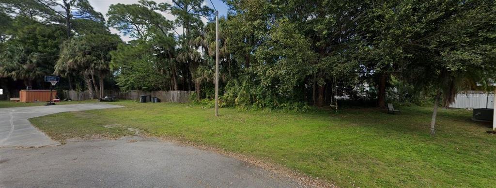 A grassy backyard features a concrete driveway, a basketball hoop, and a wooden fence — 1826 BEACHWOOD DRIVE, NORTH FORT MYERS, FL