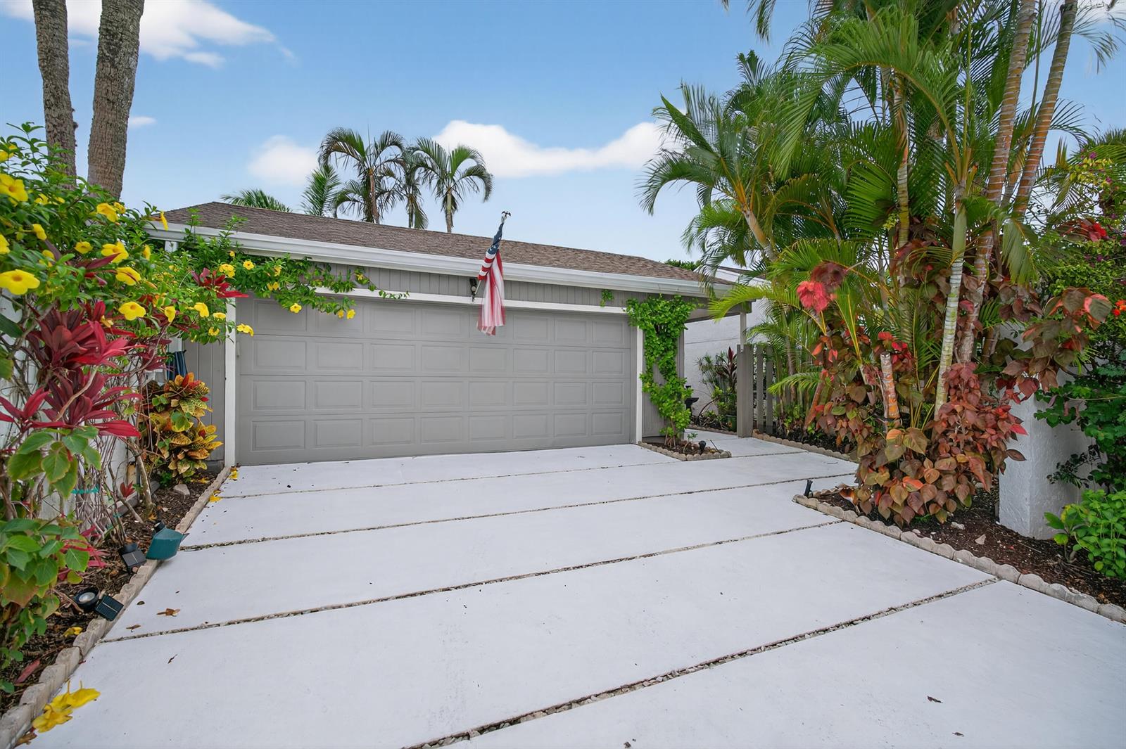 A gray garage door with an American flag sits above a concrete driveway with landscaping — 17145 Bay Street, Jupiter FL 33477, JUPITER, FL