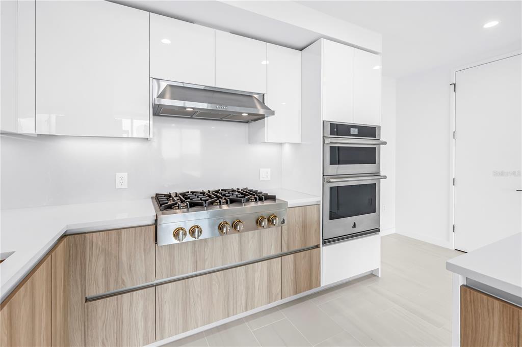 A modern kitchen features white glossy cabinets, wood-grain lower drawers, stainless steel appliances, and countertops — 400 CENTRAL AVENUE UNIT 1608, ST PETERSBURG, FL